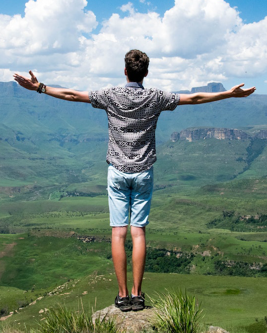 The image shows a person standing on a hilltop, with their arms outstretched, overlooking a scenic landscape.
